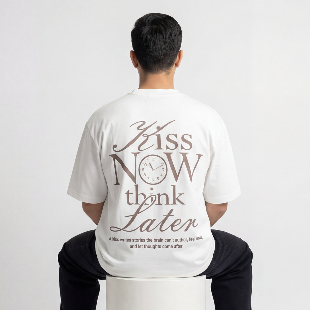 Back view of model wearing Krosso “Kiss Now Think Later” oversized antique white t-shirt with bold typography print.